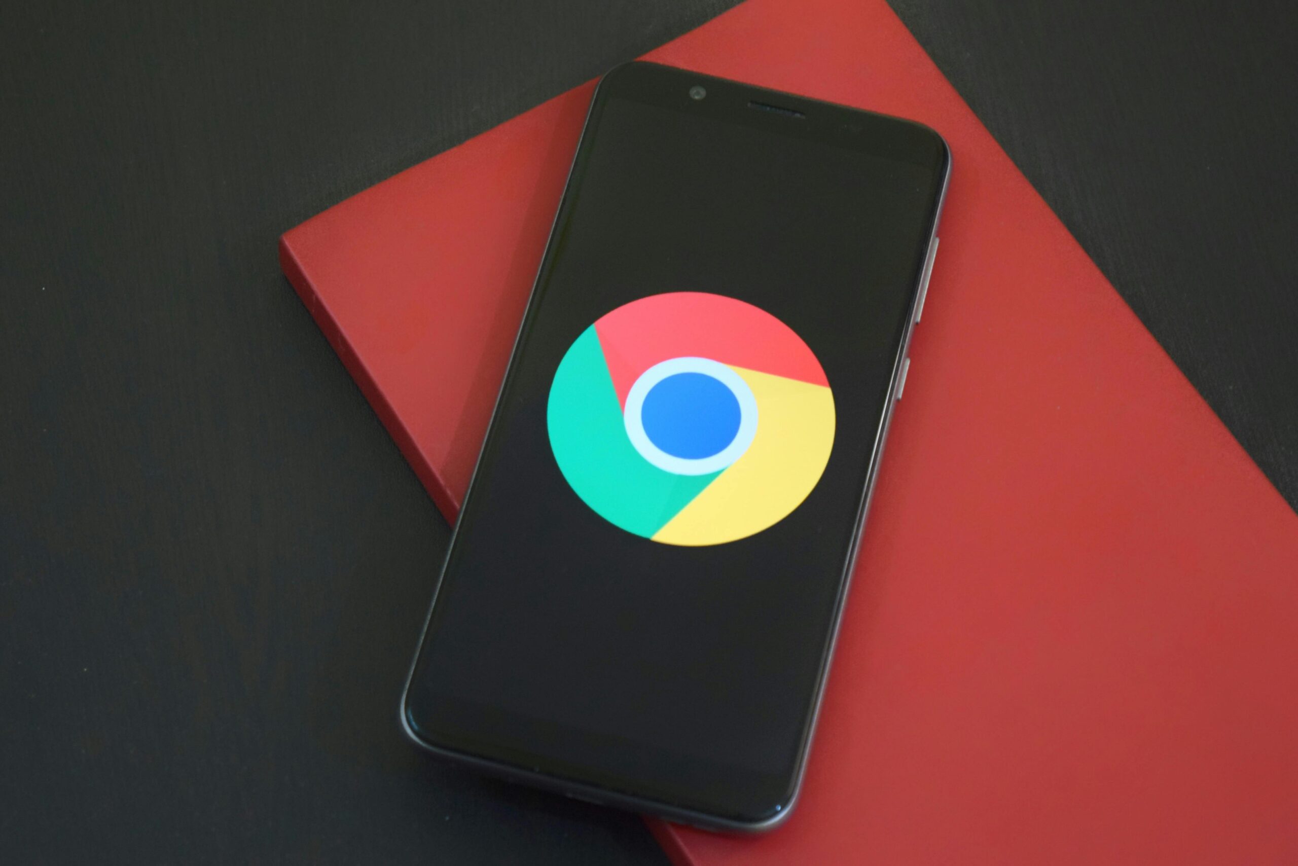 Smartphone displaying the Google Chrome logo on screen, resting on a red surface